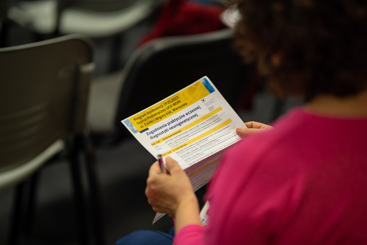 Zbliżenie. Kobieta w różowej bluzce siedzi i trzyma w ręku kartkę z programem konferencji.