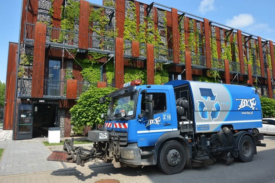 Blue tanker standing in the street in front of a large rust-coloured building covered with vegetation