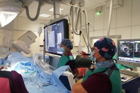 Operating theatre. Two doctors in surgical gowns caps and masks. They operate using modern apparatus.