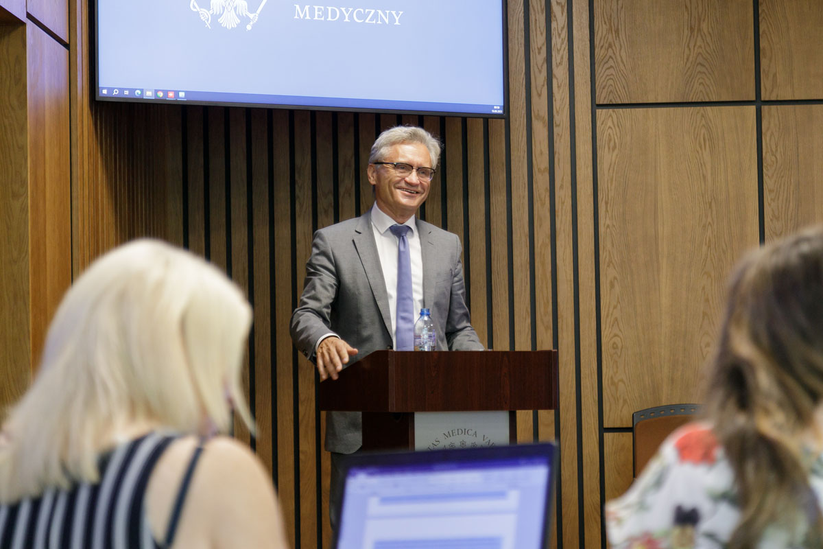 A man in a gray suit at the lectern. A screen behind him.