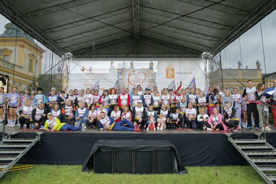 On the stage, a crowd of people wearing T-shirts with starting numbers and with Nordic walking poles in their hands in their arms