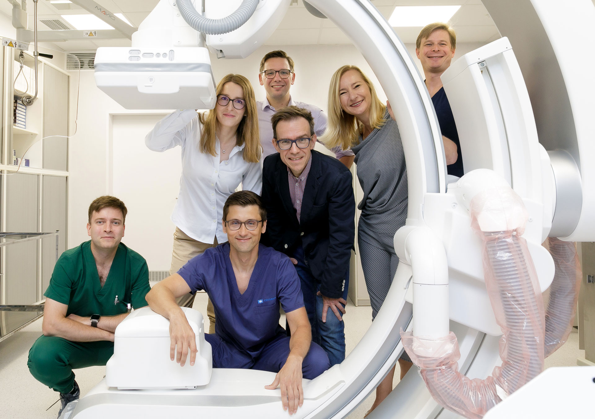 Grupa osób ubranych w stroje medyczne pozuje do zdjęcia w pomieszczeniu medycznym, przy rezonansie magnetycznym