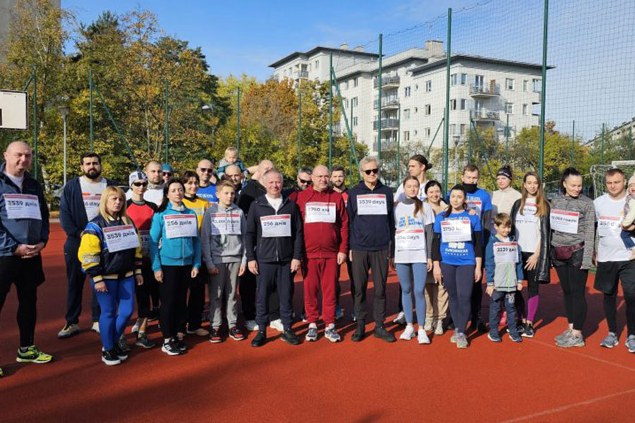 Grupa osób ubranych w stroje sportowe. Stoją na boisku i uśmiechają się do aparatu.