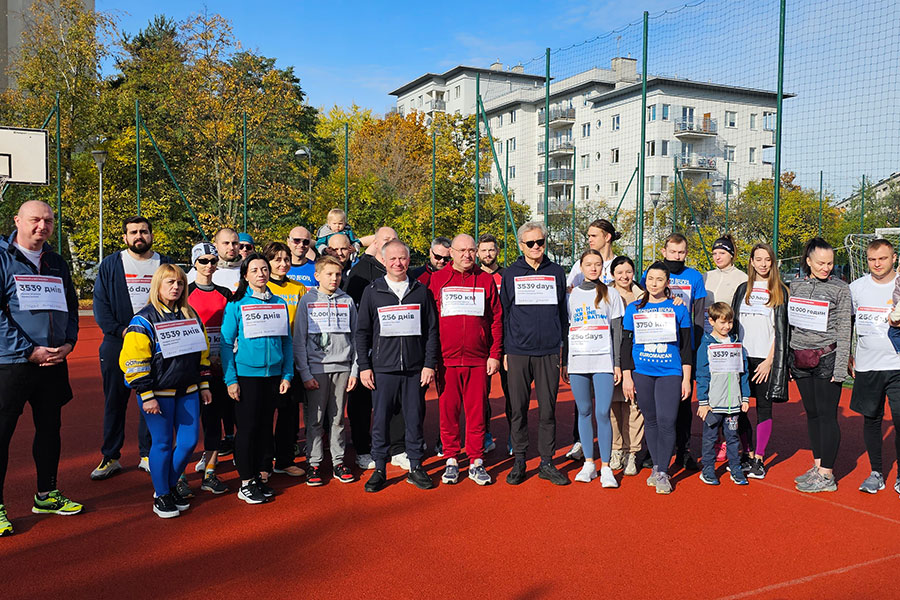 Grupa osób ubranych w stroje sportowe. Stoją na boisku i uśmiechają się do aparatu.