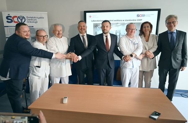Eight people pose for a photo, holding hands, some wearing medical gowns, some dressed in suits.