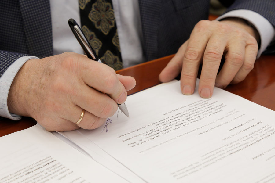 Na zdjęciu widać ręce podpisujące dokument.