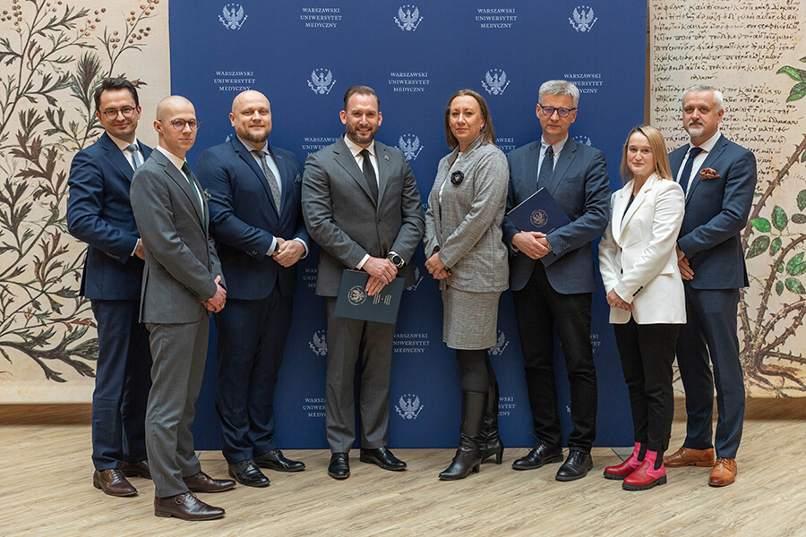 Group of elegantly dressed people, stand against blue wall, smile at camera