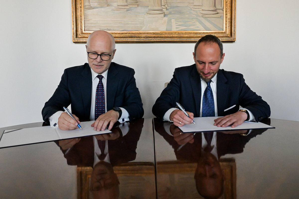 Two men in suits are sitting at a table signing documents.