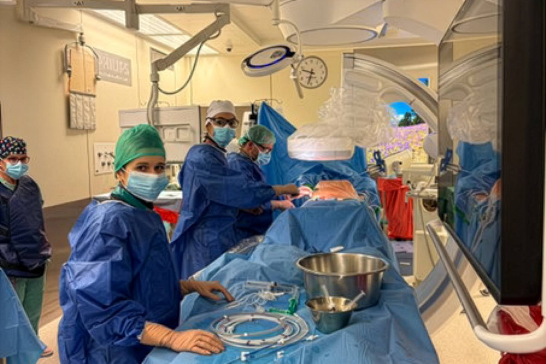 Zespół personelu medycznego w sali operacyjnej prowadzi zabieg przy stole zabiegowym, otoczony sprzętem chirurgicznym i monitorem medycznym.