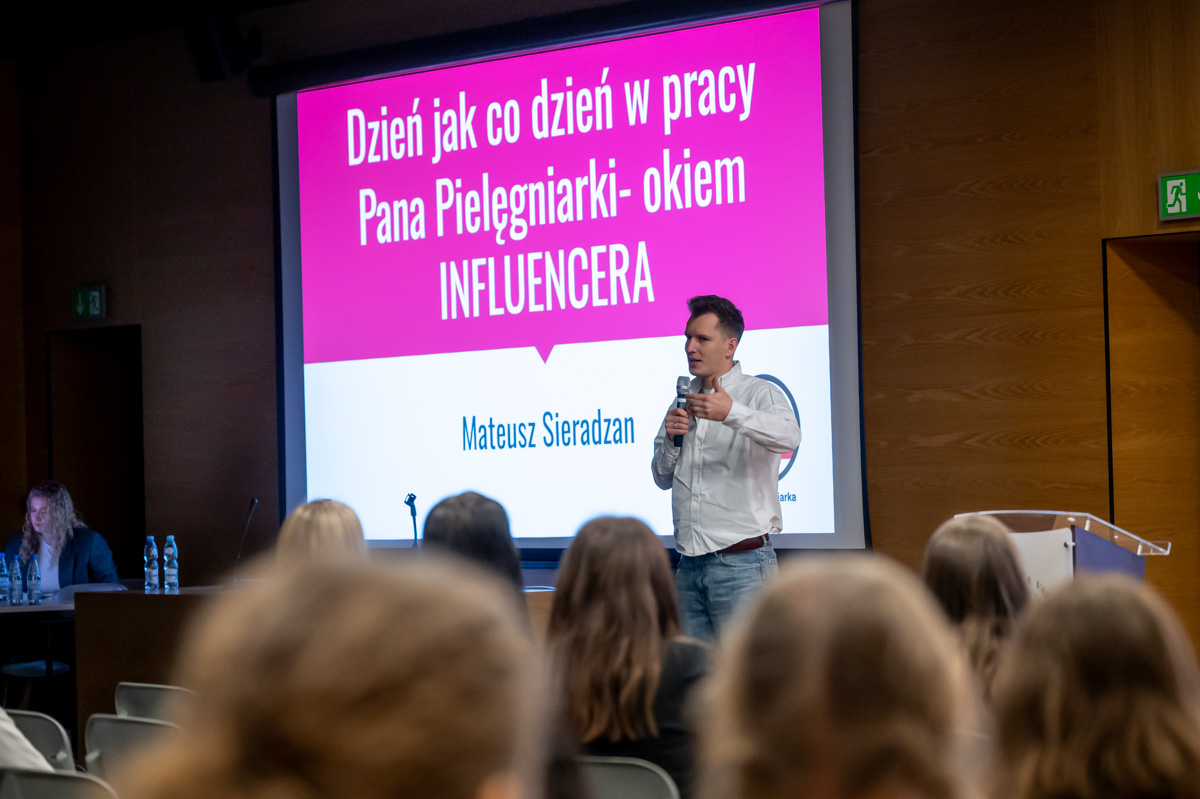 Prelegent stojący przed publicznością prowadzi prezentację na temat codziennej pracy pielęgniarza z perspektywy influencera, wyświetlaną na dużym ekranie w sali konferencyjnej.
