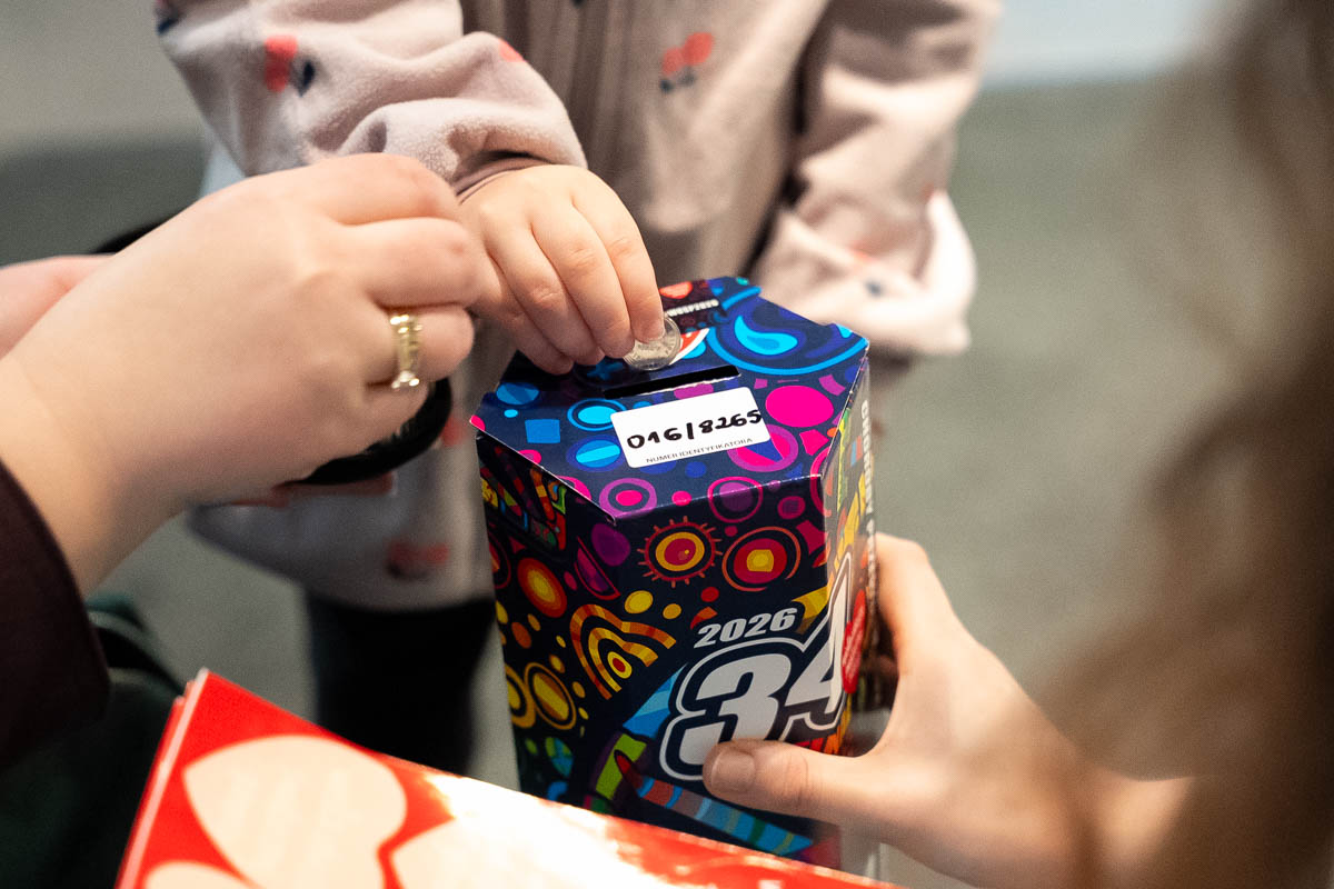 A child is putting a coin into the colourful collection can of the 34th Grand Finale of the Great Orchestra of Christmas Charity, held by an adult