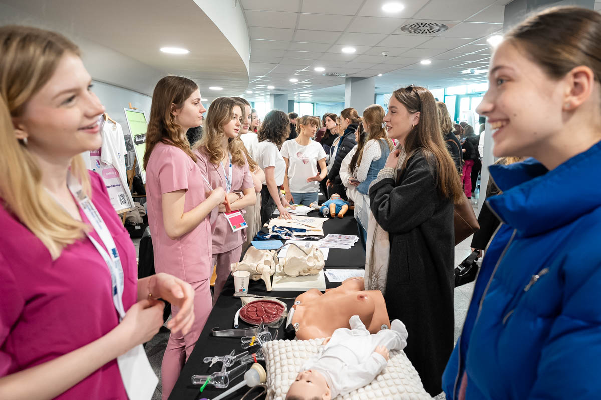 Participants of the educational event gathered at a booth presenting medical equipment and training models, engaging in conversations and demonstrations.