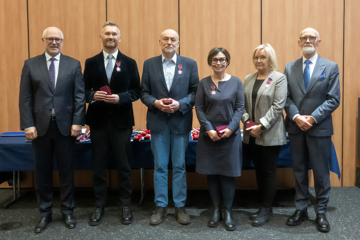 A group of people is posing for a group photo. They are dressed formally. Four people in the center are wearing pinned decorations.