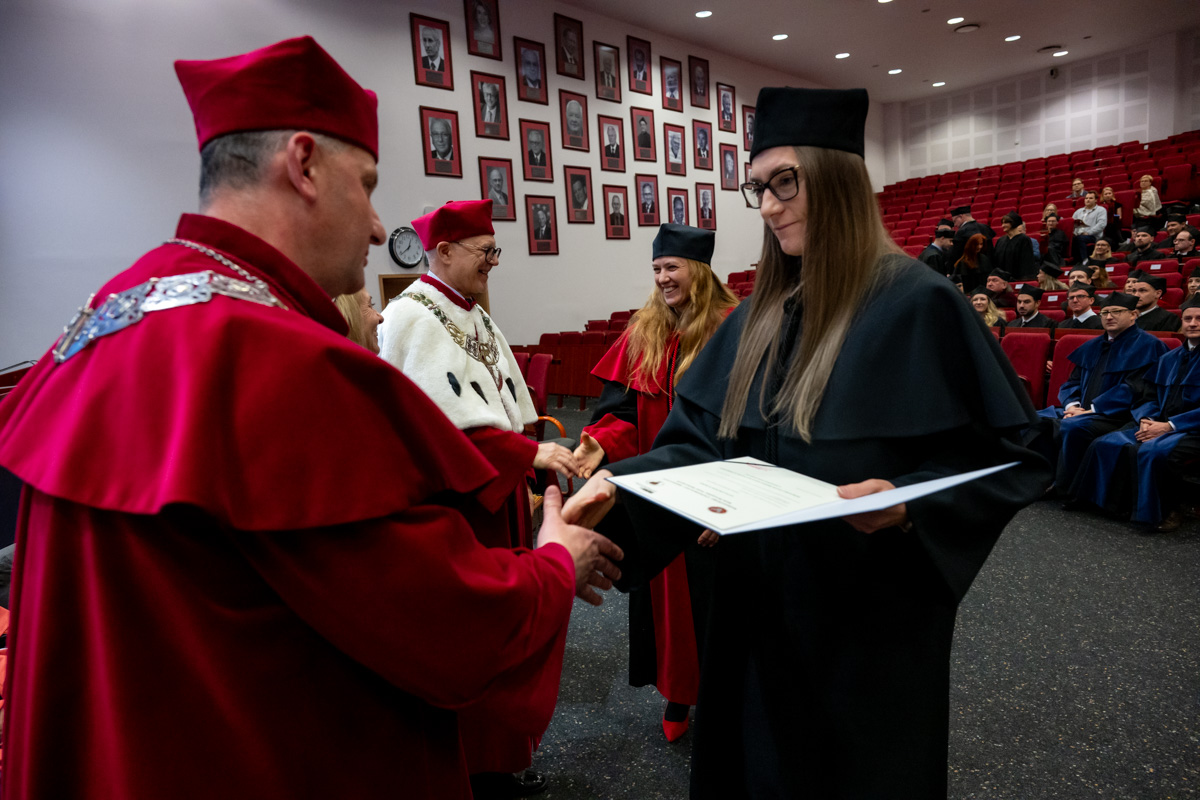 A ceremonial awarding of the diploma during an academic ceremony in the auditorium, in the presence of university authorities and the audience.