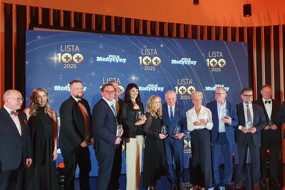 Grupa osób stojących na scenie podczas uroczystej gali „Lista 100 Pulsu Medycyny 2025”, trzymających statuetki wyróżnienia na tle ściany z logo wydarzenia.