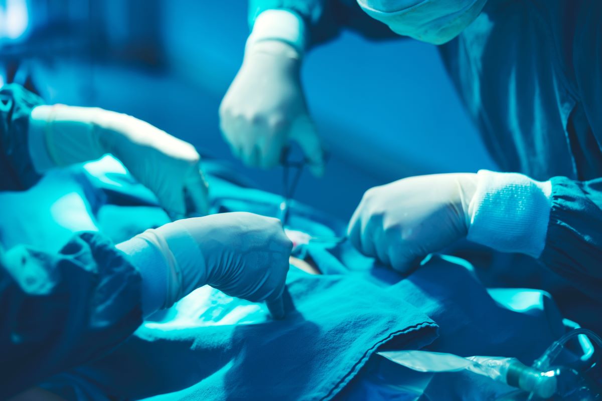 Close-up of the surgical team’s hands performing an operation in a sterile, blue-lit surgical field.