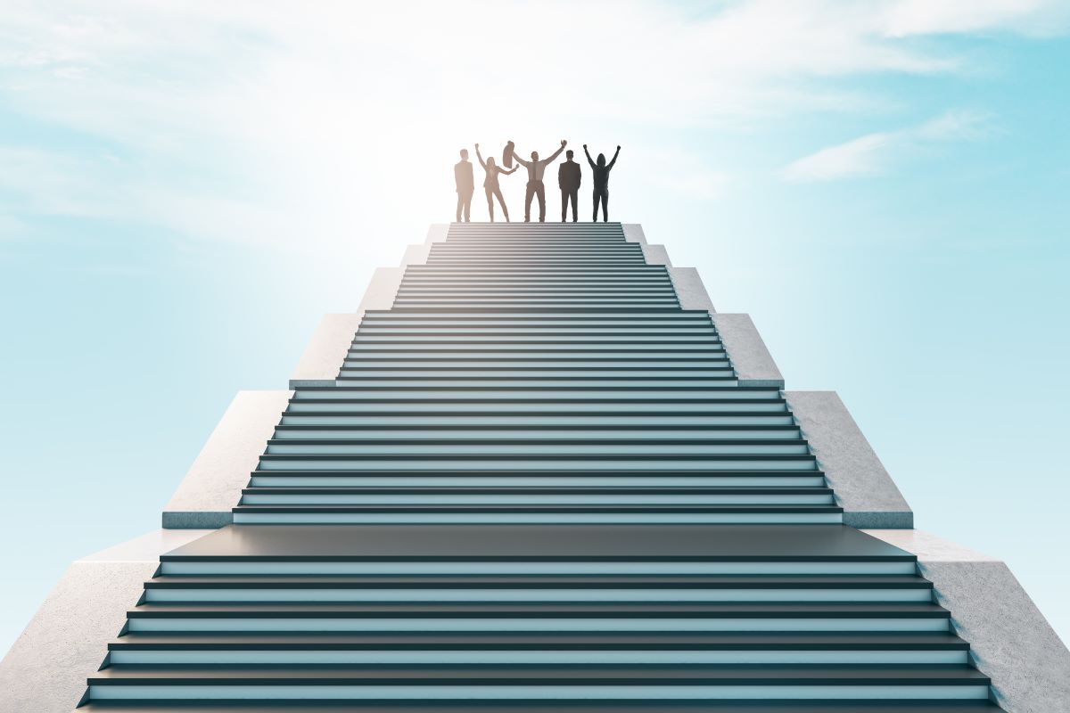 Silhouettes of several people stand at the top of wide stairs leading upward. The stairs form a symmetrical composition, and the figures raise their hands above their heads. In the background, a bright sky with clouds is visible, giving the scene a symbolic and spatial character.