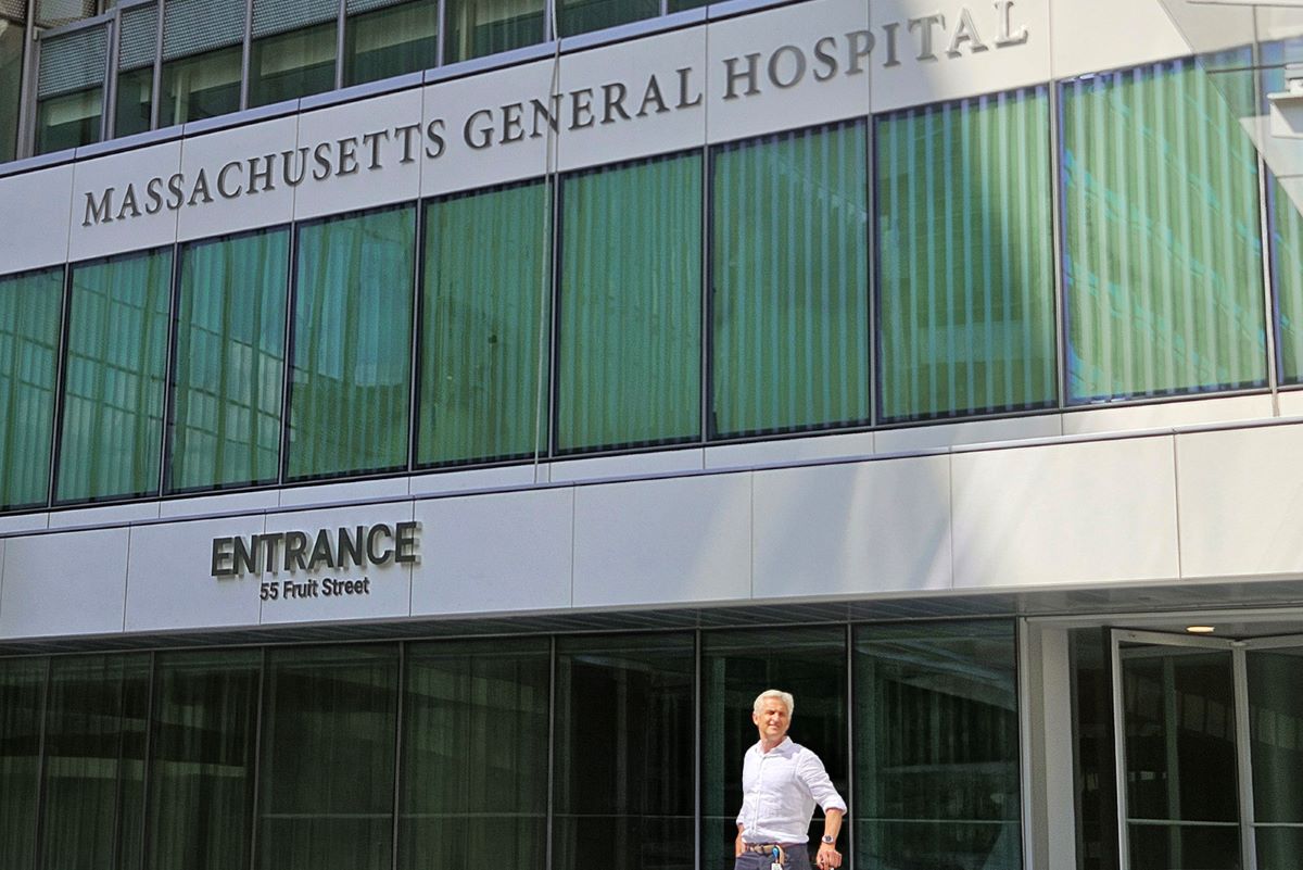 Osoba stoi przed wejściem do budynku Massachusetts General Hospital. Nad wejściem widoczne są nazwa szpitala oraz oznaczenie adresu „55 Fruit Street”.