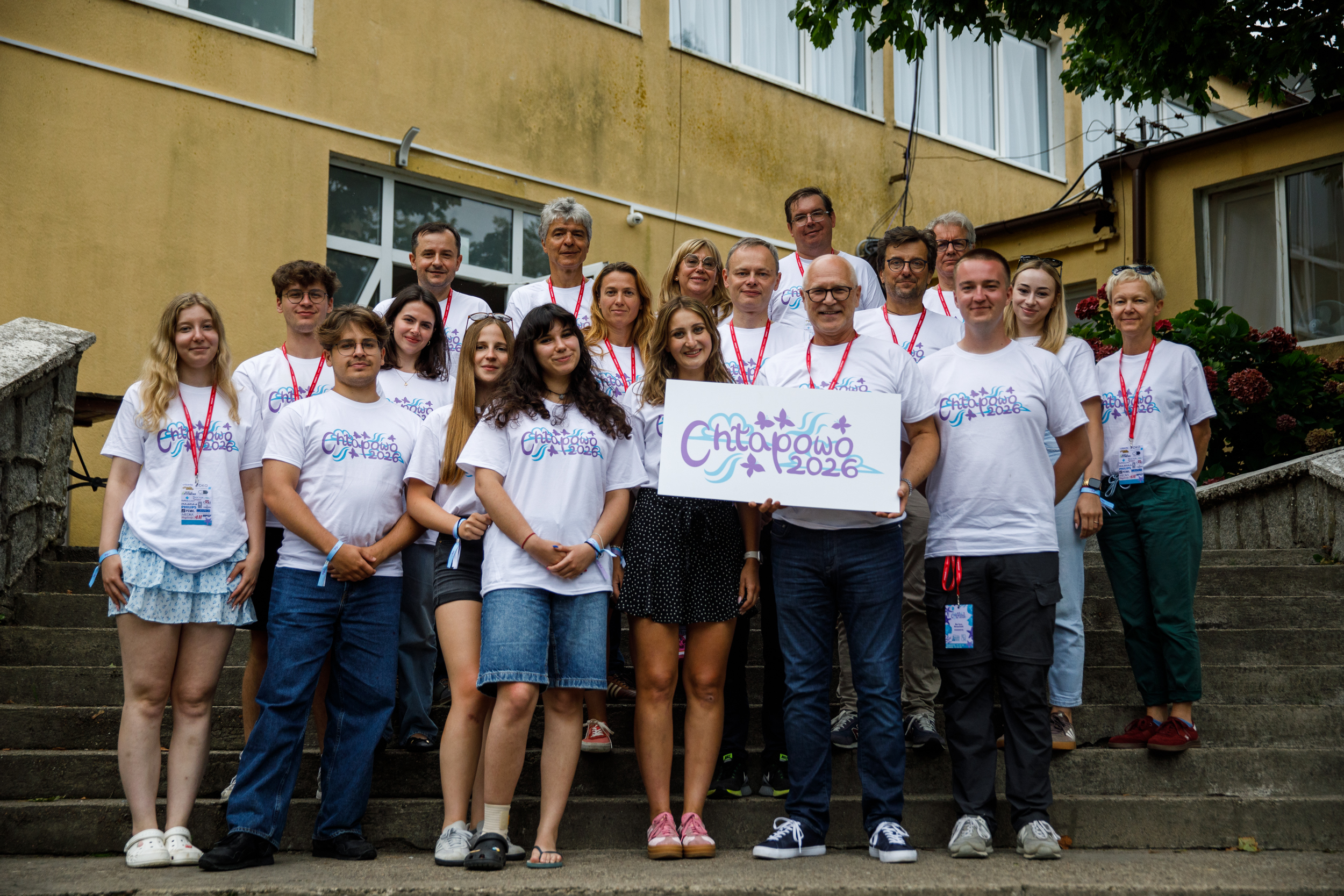 Grupa 18 uczestników wydarzenia stoi na schodach przed budynkiem. Kilka osób trzyma tablicę z napisem „Chłapowo 2026”.