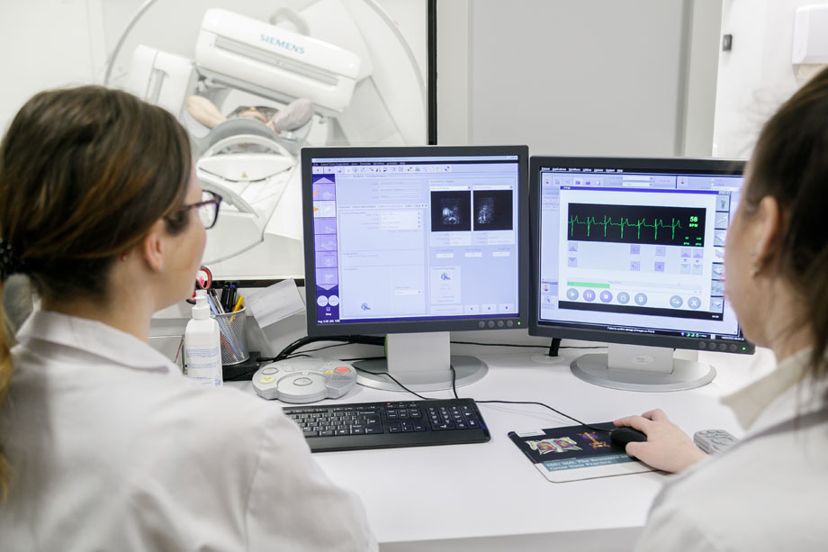Dwie studentki siedzą przy ekranach komputerowych, na których wyświetlają się badania radiologiczne. W tle widać rezonans.