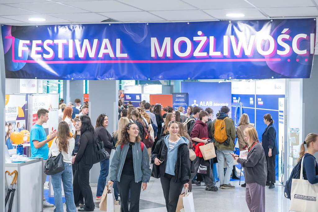 Widok ogólny tłumnego korytarza podczas targów „Festiwal Możliwości”. Nad przejściem wisi duży niebieski baner z napisem „FESTIWAL MOŻLIWOŚCI”, a w tle widać liczne stoiska wystawiennicze i spacerujących uczestników.