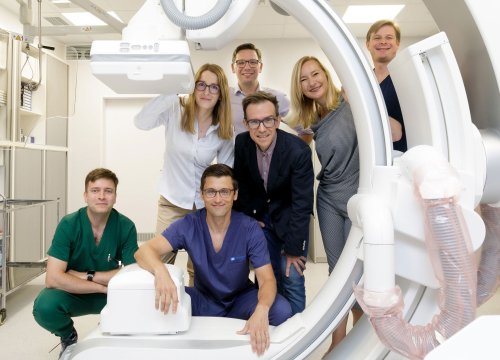Grupa osób pozująca do zdjęcia w pomieszczeniu medycznym. Stoją obok urządzenia do rezonansu magnetycznego.