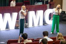 Dwie studentki śpiewają przed publicznością. Za nimi neon z napisem WIMC.