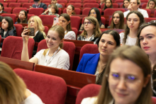 Kilkanaście osób - uczestników konferencji. Siedzą na auli konferencyjnej na czerwonych fotelach.