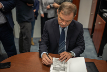 A man sits at a table and signs a book.