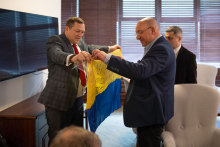 Two men. One hands the flag of Ukraine to the other.