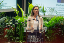 A woman at the lectern. Green palm trees in the background.