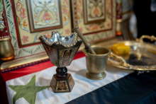 Chalice, mortar and tray on a table covered with the Syrian flag.