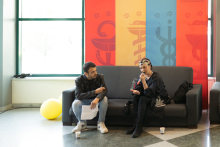 On the couch, a student is interviewing a woman dressed in dark clothing.