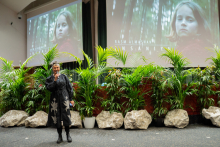 A woman in a dark outfit sings on stage. Behind her on two screens a photo of a child against a forest background.