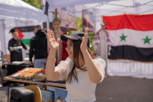 A young girl wearing a black baseball cap with Syria written on it. The girl claps her hands.