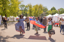 Three dark-skinned students dressed in colorful dresses carry Haiti flag