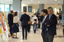 Exhibit. In the foreground on the left two men in suits. They are looking at the works on display. in the background other visitors to the exhibition.