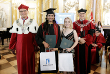 A group of four people standing. Two men and two young women. The women are standing in the middle. They hold gift bags and briefcases in their hands. 