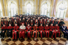 Group of people. They are seated. Most of them wearing black togas and birettas, a few in the front rows wearing black and red togas. They pose for a photo.