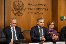 A woman and two men are sitting at a conference table. One of them is speaking into the microphone.