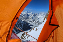Widok z pomarańczowego namiotu na ośnieżone pasma górskie. W tle niebieskie niebo.