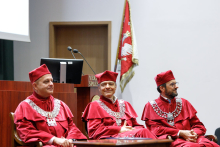 Uroczystość wręczenia dyplomów ukończenia studiów. Władze uczelni. Trzech mężczyzn (prorektorzy) w czerwonych togach i biretach.