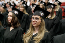 Uroczystość wręczenia dyplomów ukończenia studiów. Młodzi ludzie w czarnych togach i biretach.