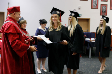 Mężczyzna (prorektor) w czerwonej todze wręcza absolwentom dyplomy.