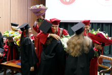 Absolwenci wręczają kwiaty mężczyznom (prorektorom) ubranym w czerwone togi.