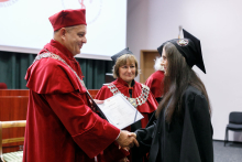 A man (pro-rector) in a red toga presents diplomas to graduates.