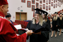 A man (pro-rector) in a red toga presents diplomas to graduates.