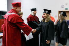 A man (pro-rector) in a red toga presents diplomas to graduates.