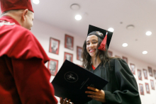 A man (pro-rector) in a red toga presents diplomas to graduates.