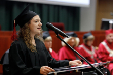 A graduate in a black toga speaks into the microphone.